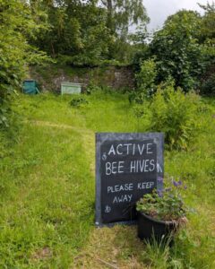 A sign in a country garden says 'Active beehives, keep away'. A beehive can be seen in the background