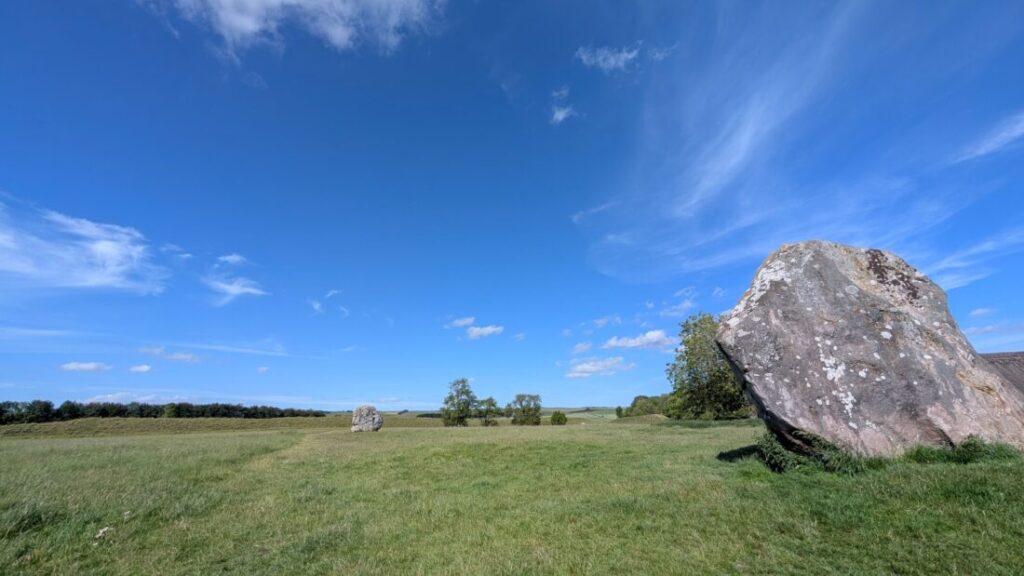 Two Neolithic standing stones in a field under a bright blue sky.