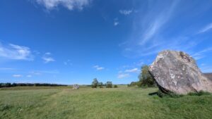 Two Neolithic standing stones in a field under a bright blue sky.