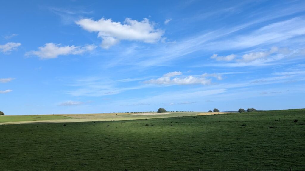 A wide sweeping view of rolling green farmland under a big blue sky with whisps of white cloud.