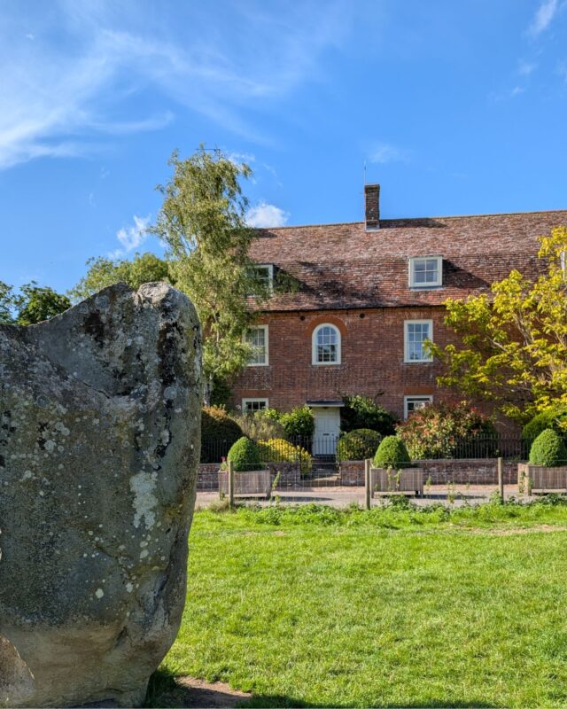 A Neolithic standing stone with a cottage in the background.