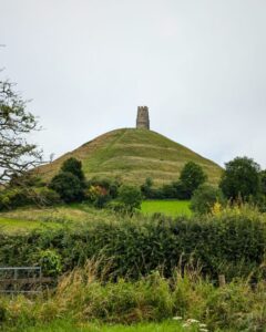 View of Glastonbury Tor from a distance with the church tower on top of the hilll, and hedges and fields in the foreground