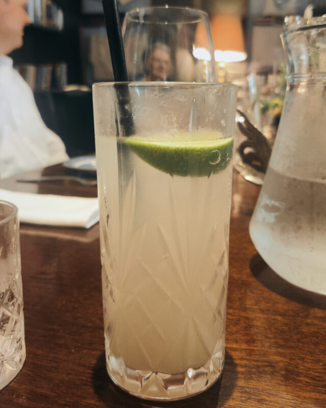 A glass of homemade ginger beer with a black straw and a slice of lime in it.
