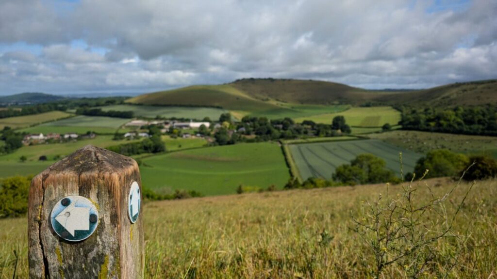 Photo of a footpath waymarker with green countryside stretching out in the background