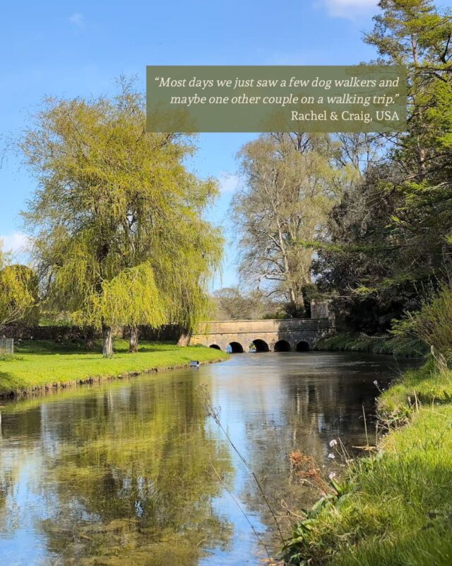 View down a wide river to an old stone bridge. It's a bright spring day and there is a guest testimonial in the top right corner "“Most days we just saw a few dog walkers and maybe one other couple on a walking trip.” Rachel & Craig, USA"