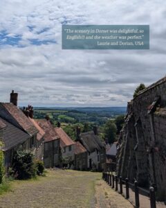 View from the top of a steep cobbled street. Ancient cottages line the left side and old castle walls can be seen on the right