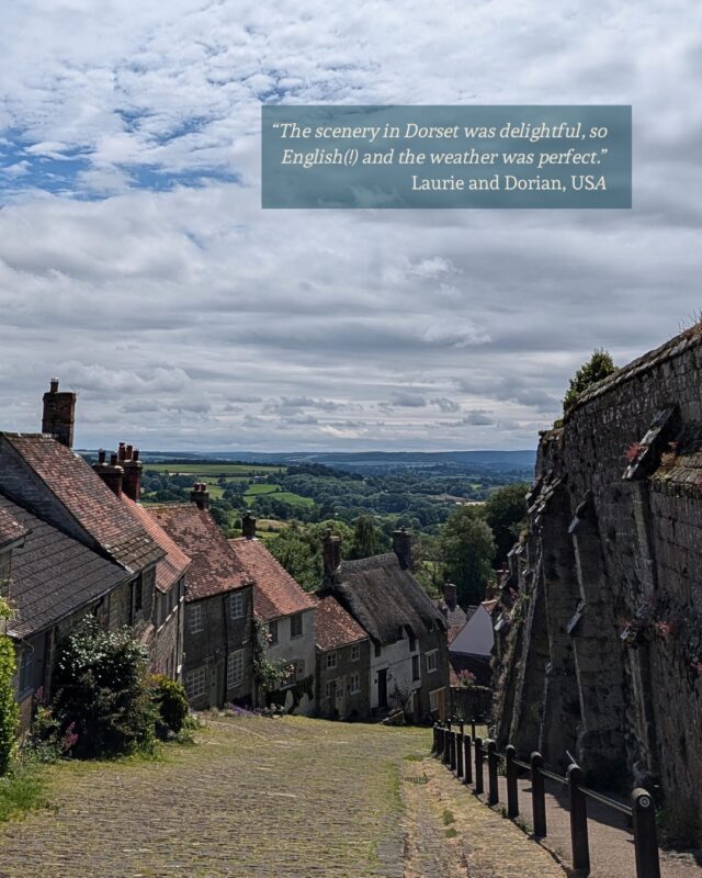 View from the top of a steep cobbled street. Ancient cottages line the left side and old castle walls can be seen on the right