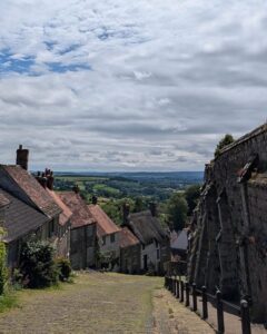 View from the top of a steep cobbled street. Ancient cottages line the left side and old castle walls can be seen on the right