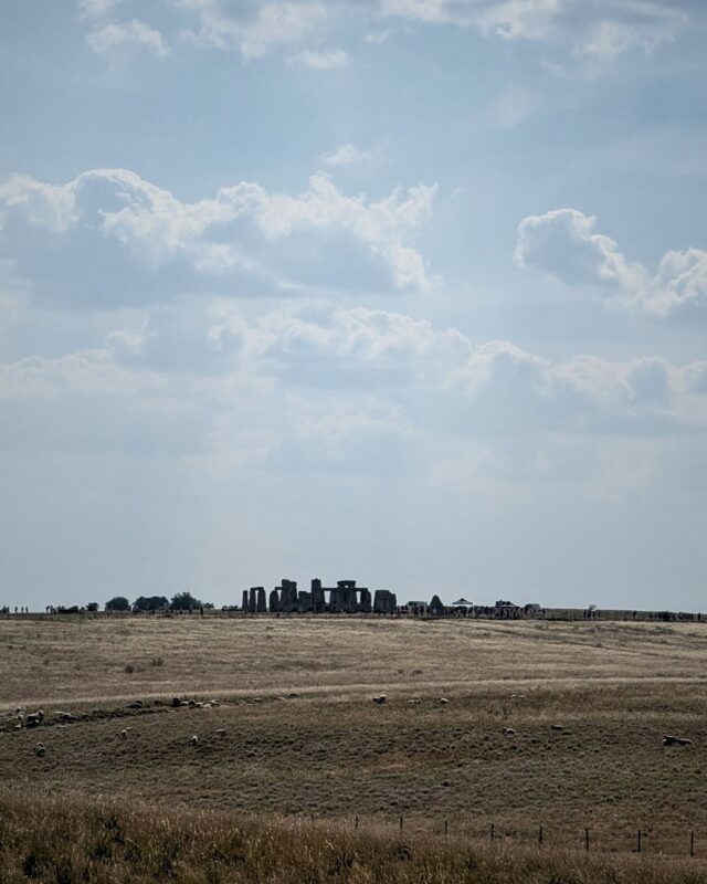 View of Stonehenge from a distance on a bright summer's day over agricultural fields.