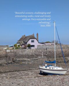 View of a boat in a harbour with the tide out and thatched cottages in the distance. A guest testimonial is shown in the top right corner: “Beautiful scenery, challenging and stimulating walks, rural and lovely settings. Very enjoyable and refreshing.” Jean, USA