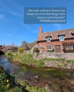 View of a red-brick cottage next to a river under a bright blue sky. There is a guest testimonial in the top right corner: “My week walking in Exmoor was simply one of the best things I have done in a very long time.” Franziska, Switzerland