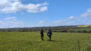 Two hikers seen from behind walking across a field and pointing at something in the distance.