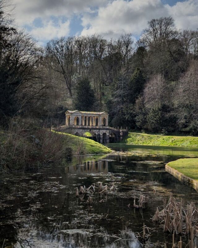 View of the Palladian bridge in Prior Park from a distance showing the river winding towards the bridge