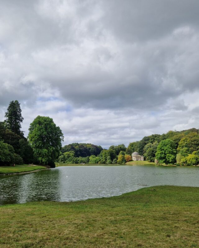 View over a lake in a grand country house garden with a temple in the distance on the other side of the lake,