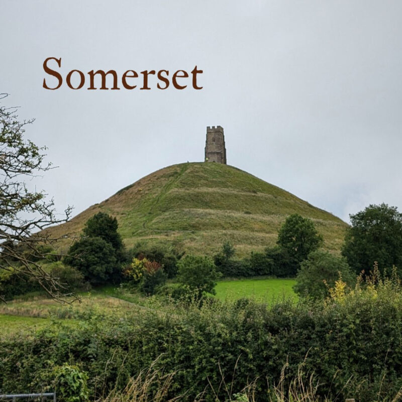 A view of Glastonbury Tor with St Michael's church tower on top silhouetted against a gey sky