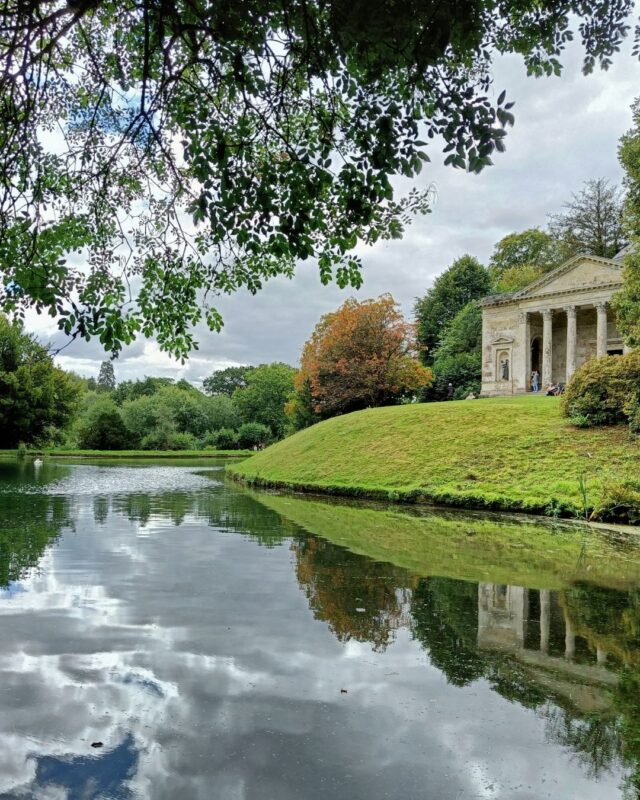 View of a replica Greek temple next to a lake taken from under a tree at the very start of autumn