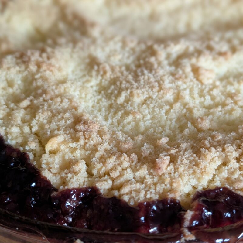 Close up of the top of an apple and blackberry crumble with the filling bubbling out and up the side.