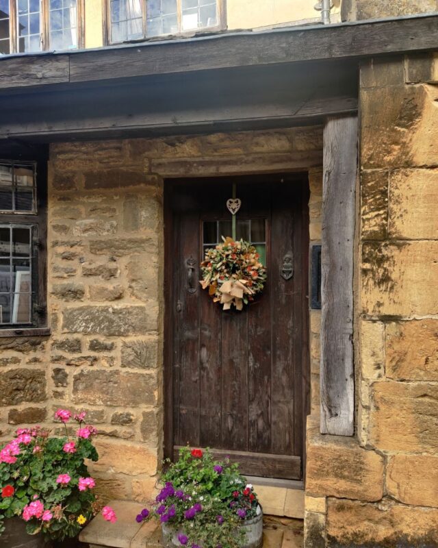 Photo of a wooden door in a stone cottage. A beautiful autumnal wreath is attached to the door.
