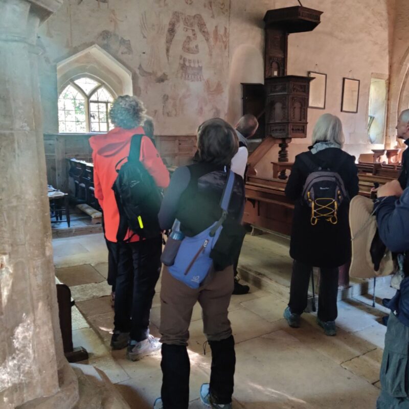 A group of hikers are standing in an ancient church looking at medieval wall paintings